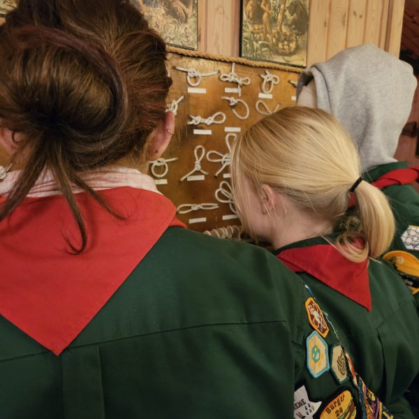 To spejderledere viser en færdselstavle for en gruppe børn